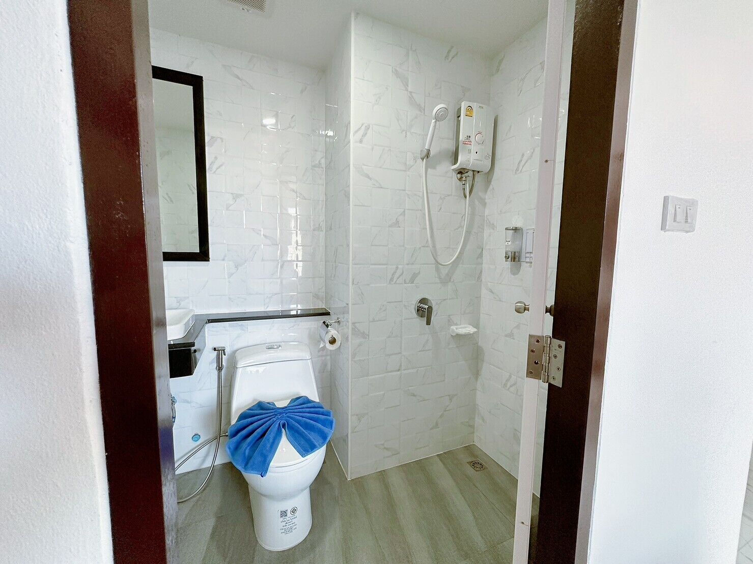 A bathroom with white marble tiles, a toilet with a blue bow, a shower with a handheld showerhead, and a wall-mounted heater.