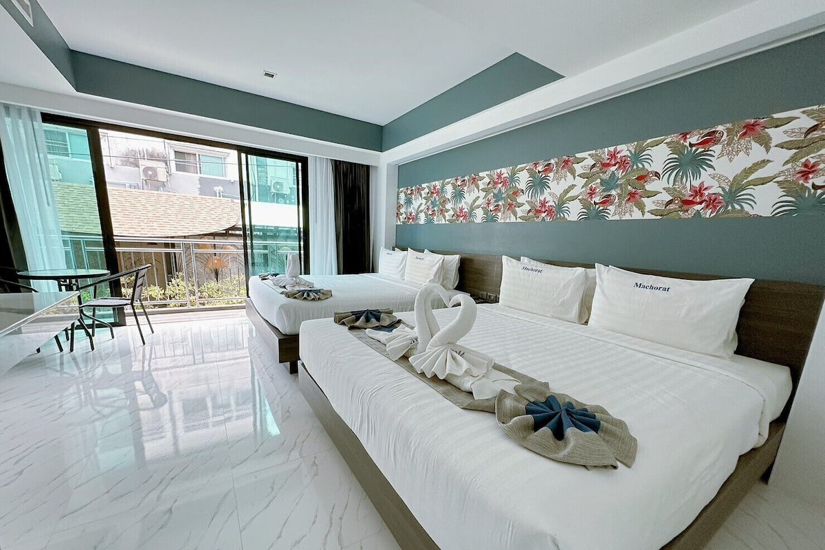 A hotel room with a large bed, a balcony with a view, and a dining area with a table and chairs.