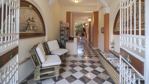A checkered floor, white cushioned seating, and a reception desk in a hallway with arches and decorative railings. - Ano Aparthotel (Corfu)