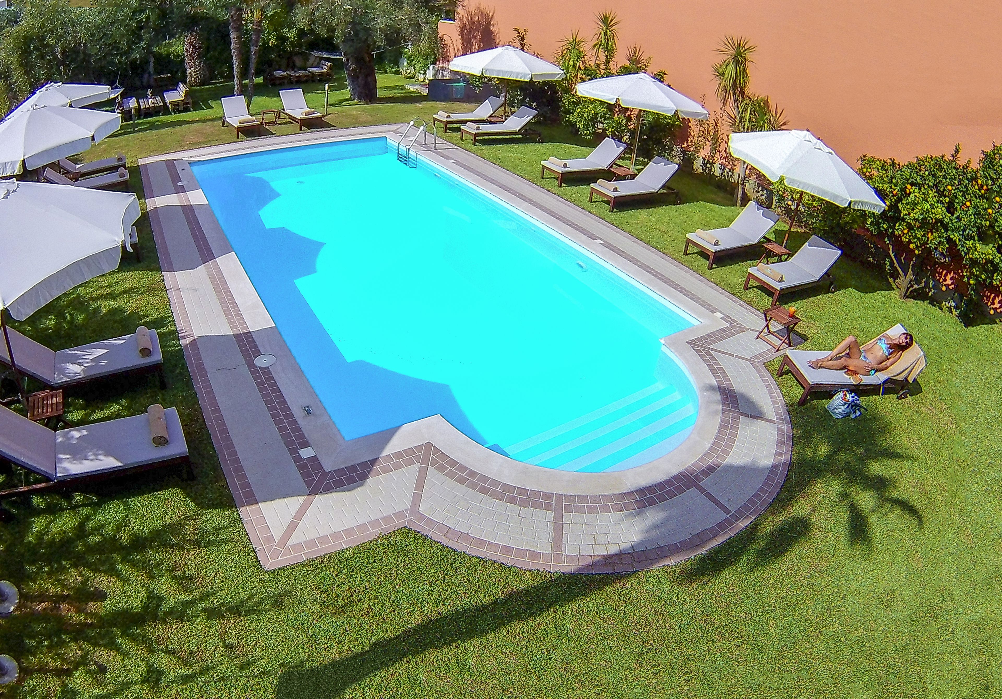 A swimming pool with lounge chairs and umbrellas, surrounded by well-maintained grass and palm trees.