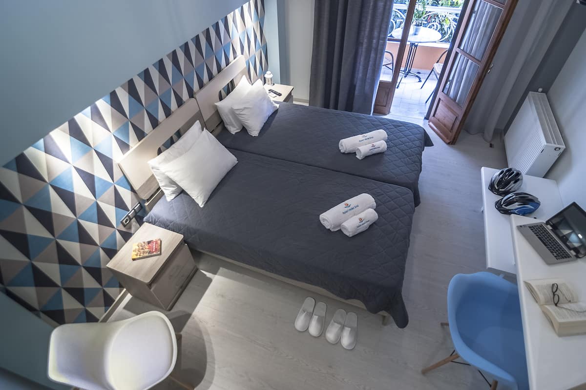 Una camera d'albergo con un letto, una scrivania con un portatile, una sedia e vista sul balcone esterno.