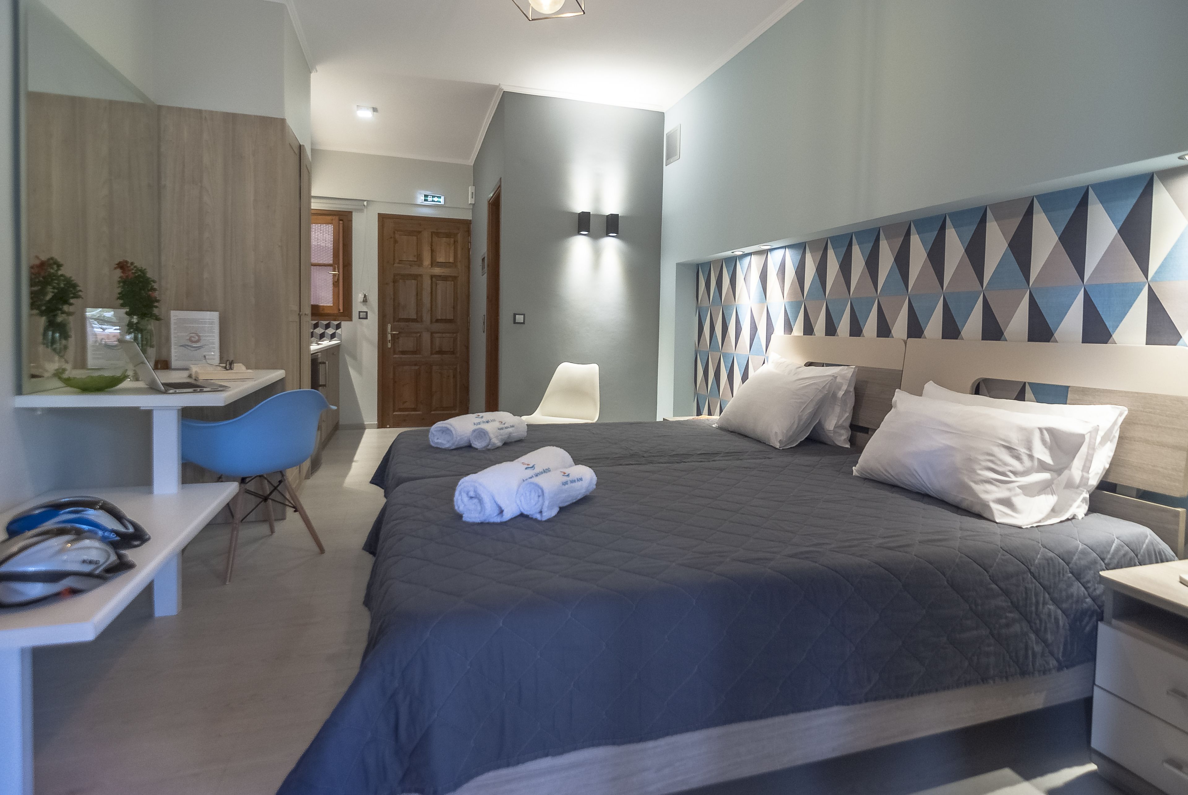 A hotel room with a bed, a desk, a chair, and a bathroom visible in the background.