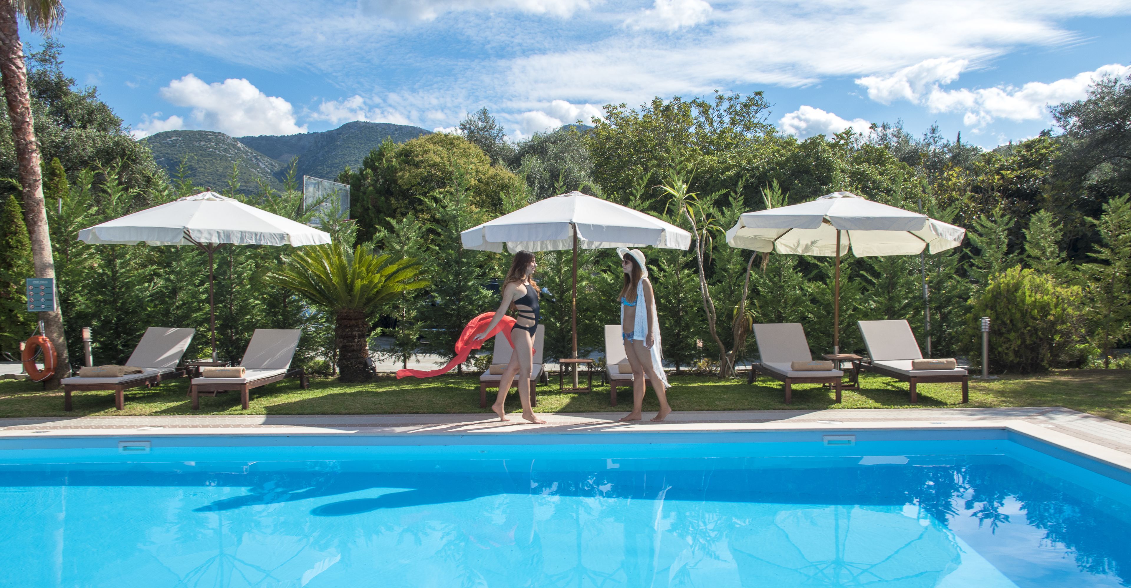 Une piscine entourée de verdure et de collines, avec des chaises longues et des parasols.