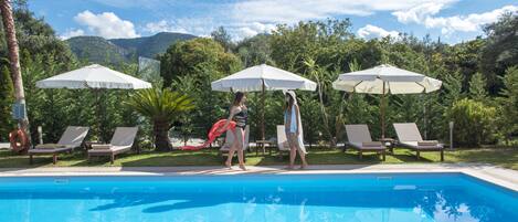 Une piscine entourée de verdure et de collines, avec des chaises longues et des parasols.