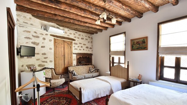 A room with a stone wall, wooden ceiling beams, a bed, a sofa, a TV, and a window with a view. - Sille Konak Hotel (Konya)
