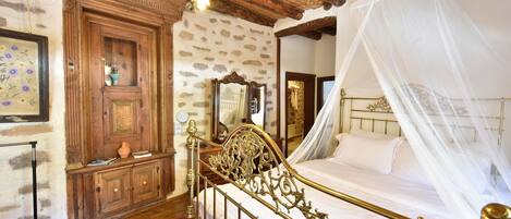 A bedroom with a bed, a wooden wardrobe, a mirror, and a red patterned rug.