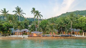 A beachfront hotel with palm trees, lounge chairs, and a pool area. - The Mud (Koh Samui)