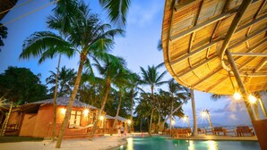 A resort with a pool, palm trees, and a thatched-roof structure. - The Mud (Koh Samui)