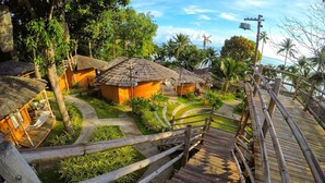 A wooden boardwalk leading to traditional huts with thatched roofs, surrounded by lush greenery and palm trees. - The Mud (Koh Samui)