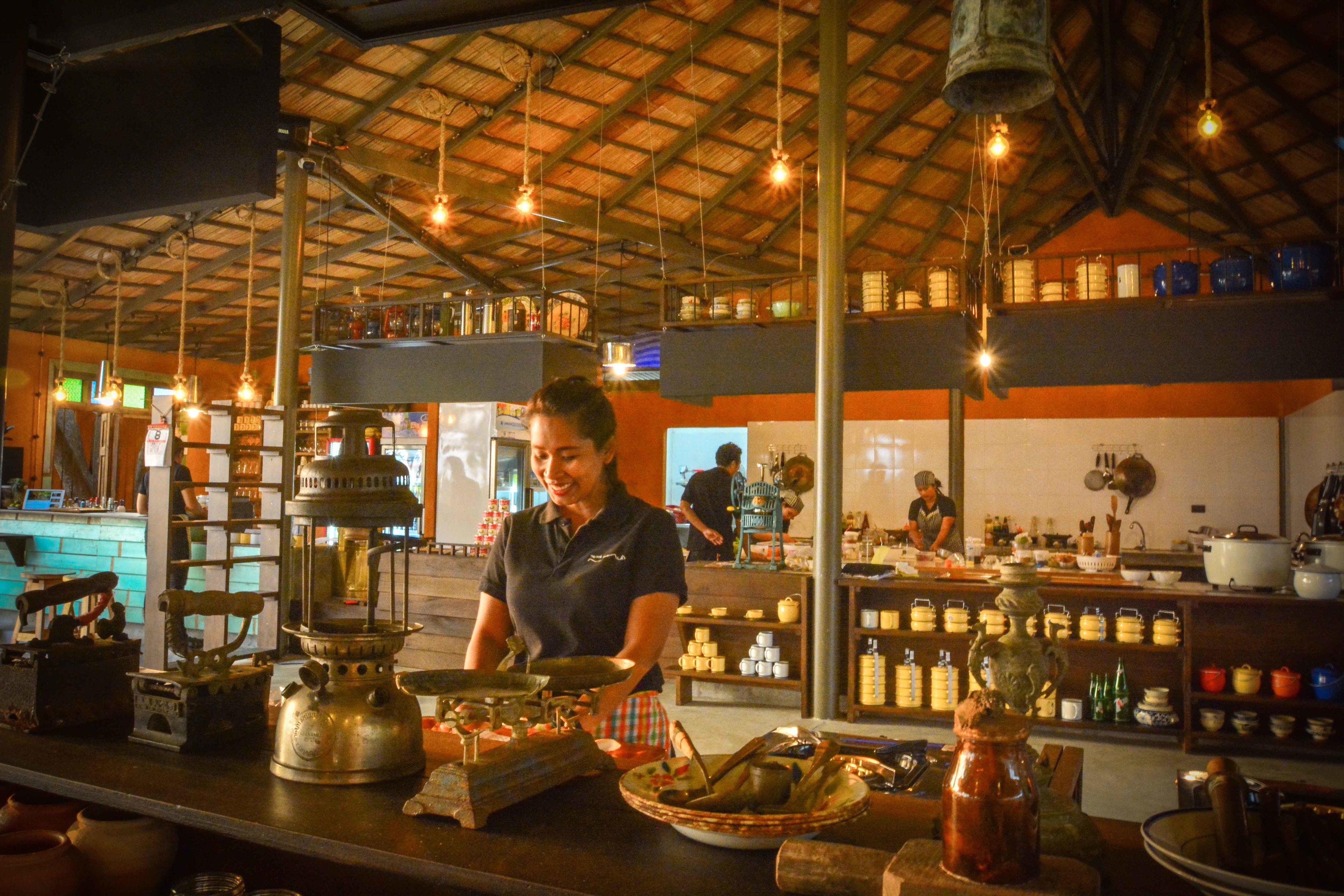 A restaurant interior with a high ceiling, hanging lights, and a variety of kitchen utensils and cookware on display.
