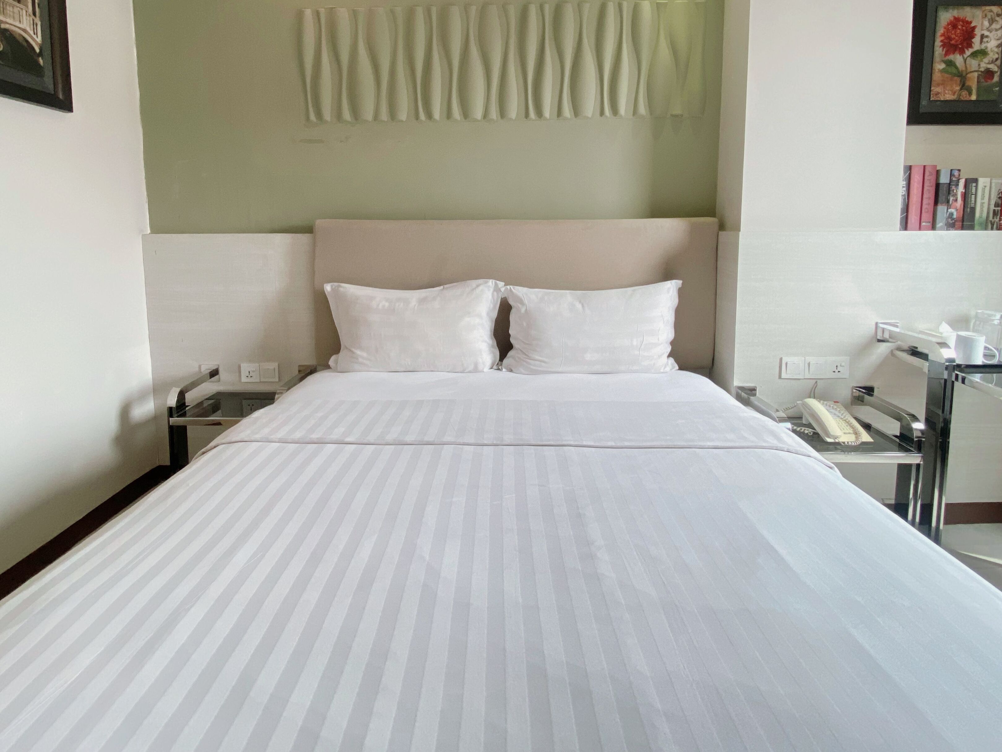 Habitación de hotel con cama, dos almohadas, mesita de noche con teléfono y lámpara de pared.