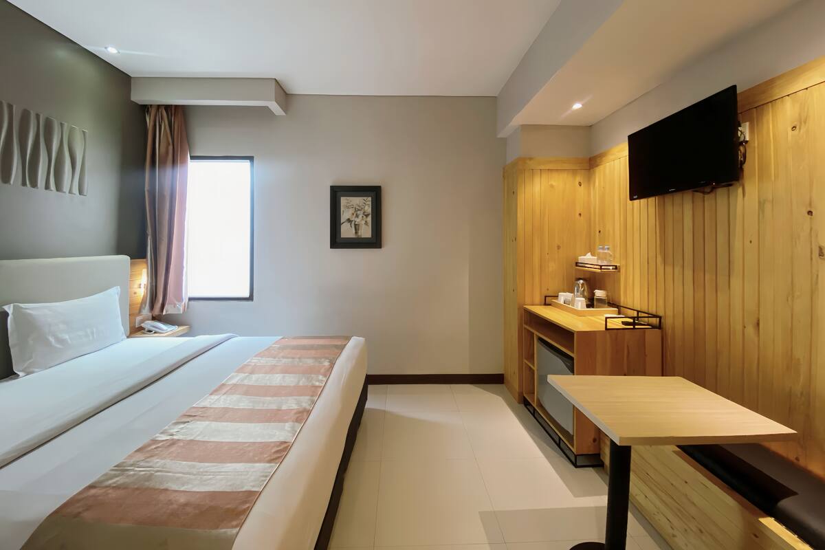 Una habitación de hotel moderna con cama, una kitchenette pequeña, un televisor y un ventanal con cortinas.