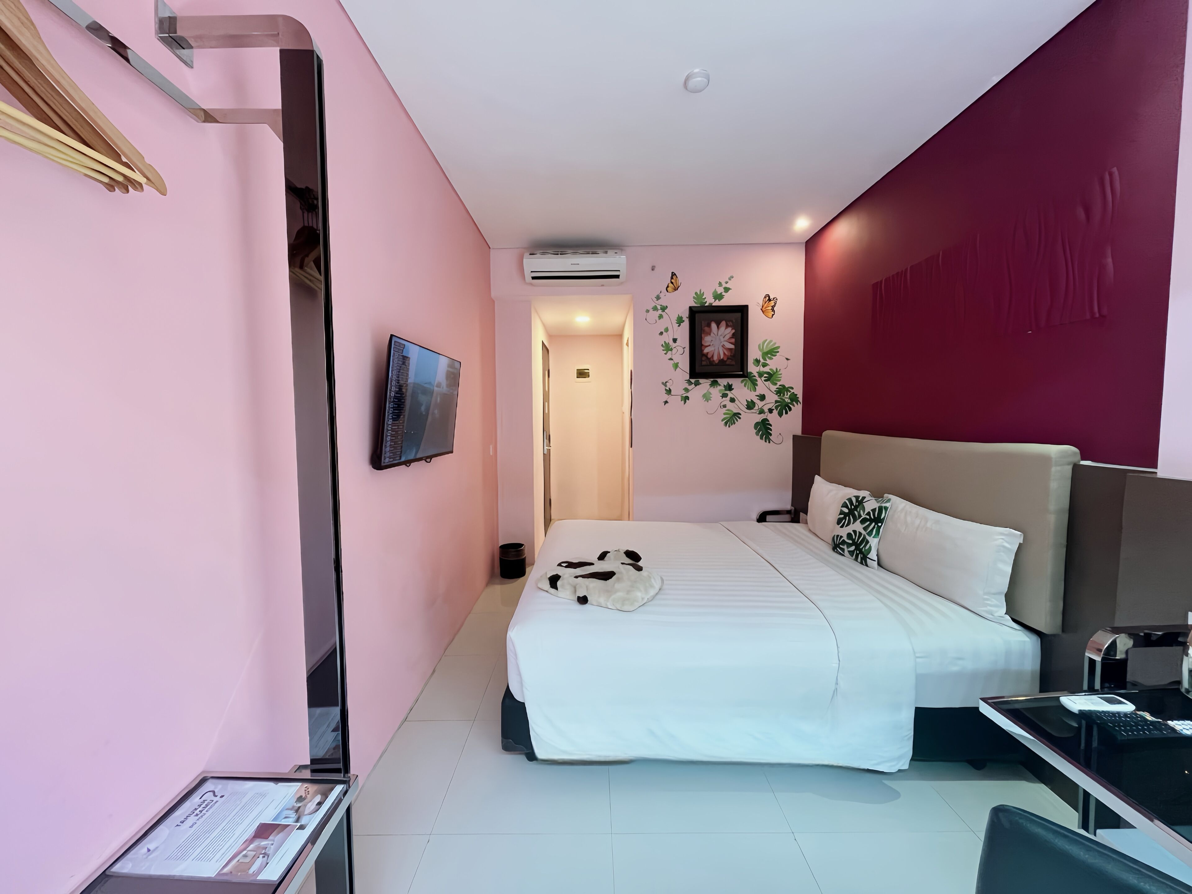 Una habitación de hotel moderna con una cama grande, un escritorio con computadora y un televisor fijado a la pared.