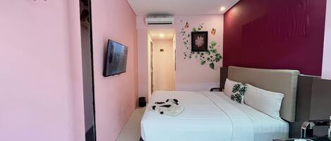 Una habitación de hotel moderna con una cama grande, un escritorio con computadora y un televisor fijado a la pared.
