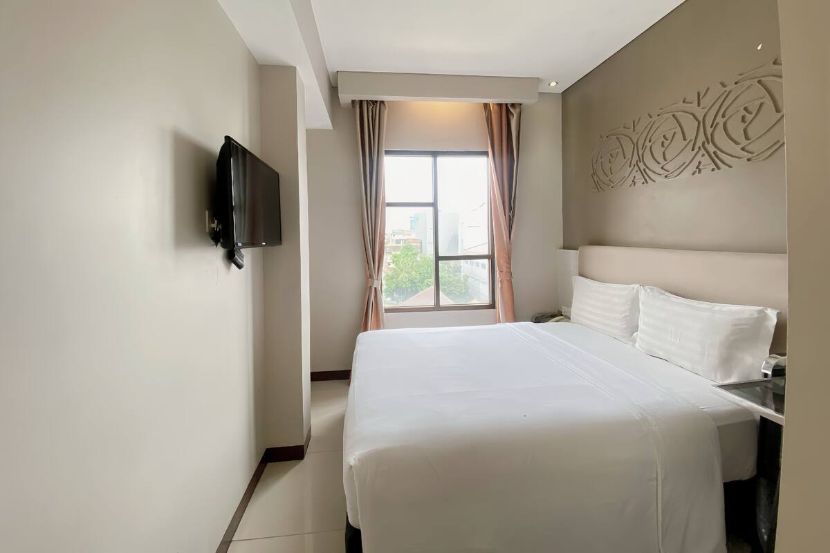 Habitación de hotel con una cama grande, televisor montado en la pared y una ventana con cortinas.