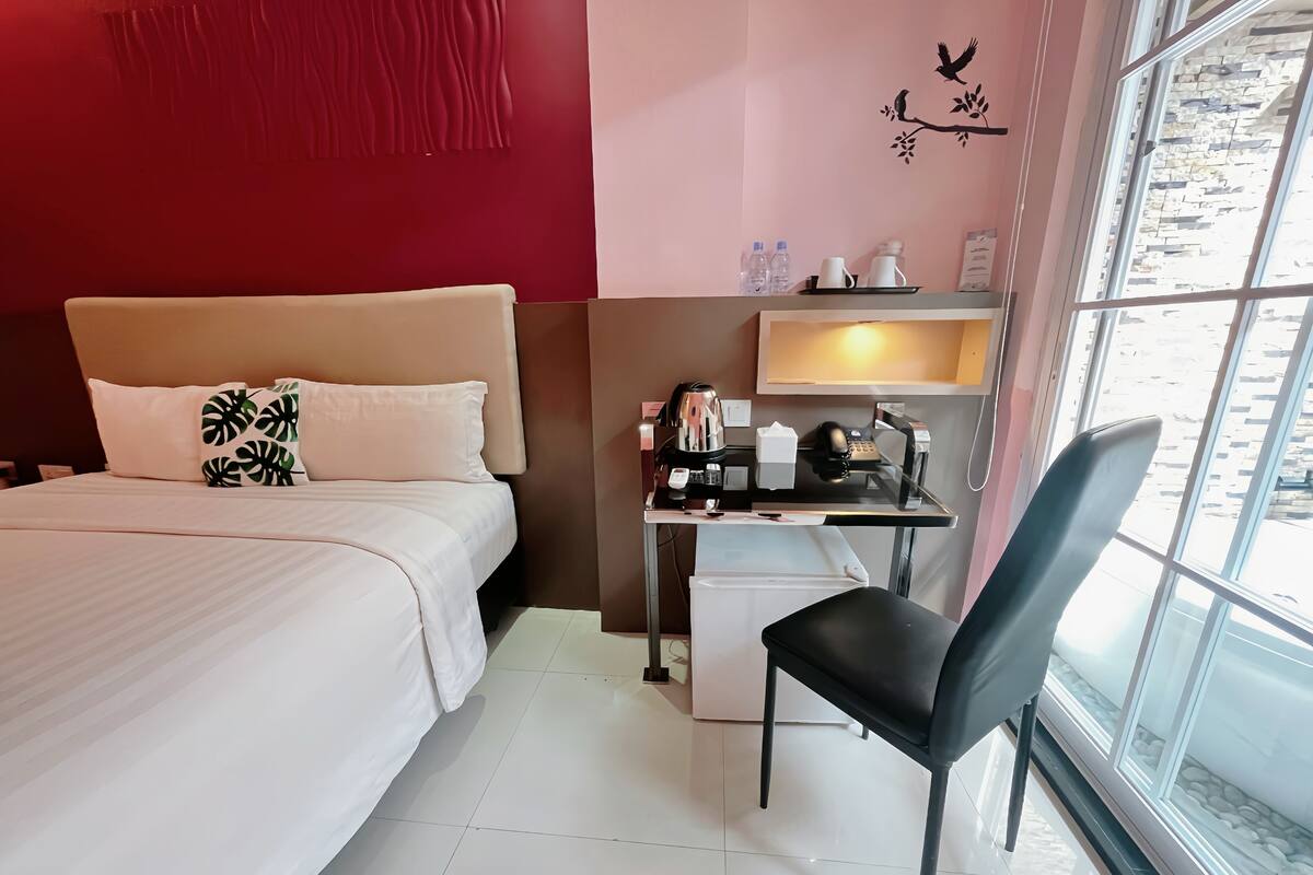 Habitación de hotel con cama, escritorio con silla, refrigerador pequeño y ventana con vista al exterior.