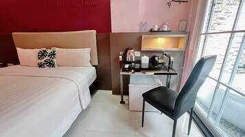 Habitación de hotel con cama, escritorio con silla, refrigerador pequeño y ventana con vista al exterior.