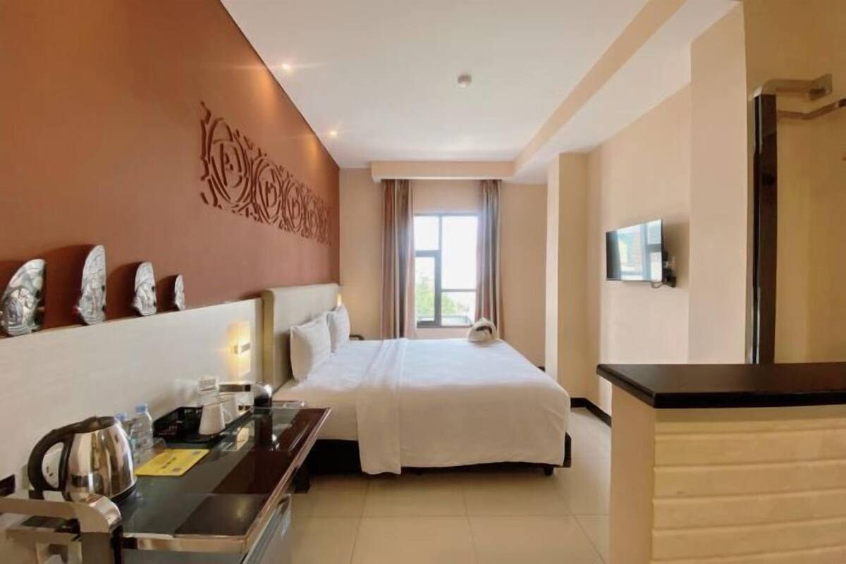 Habitación de hotel con cama, escritorio con tetera, televisor de pantalla plana y decoración en la pared.