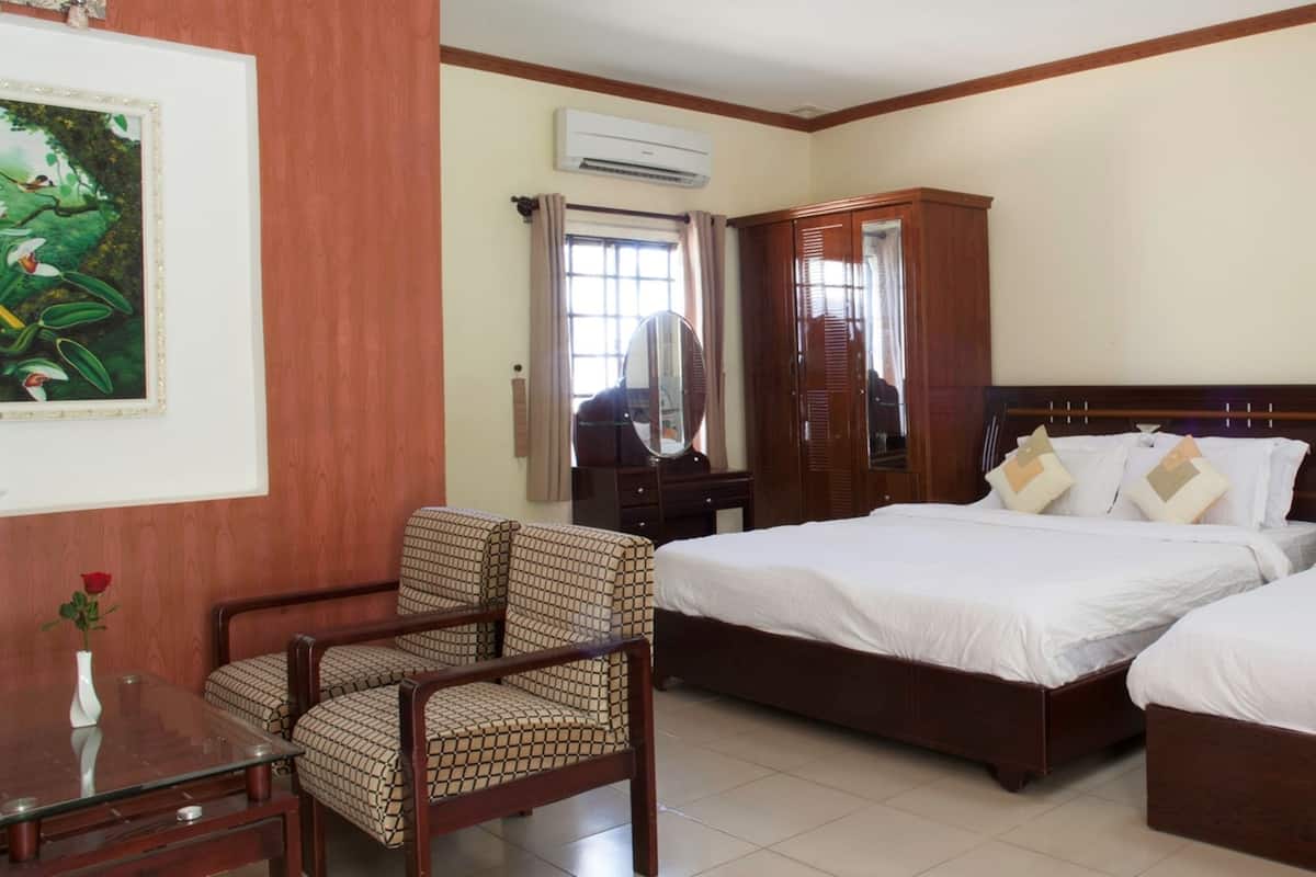 A hotel room with two beds, a wooden wardrobe, a chair, a table with a vase, and a painting on the wall.