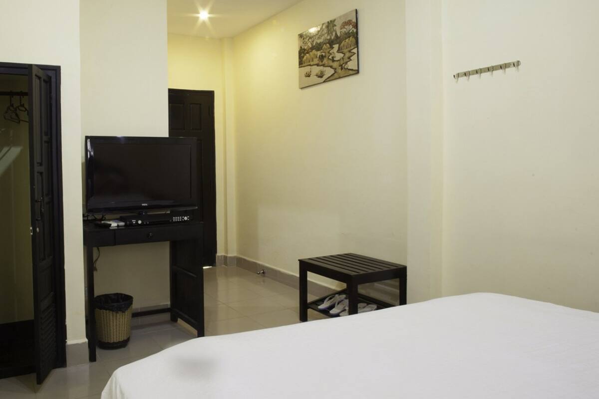 A hotel room with a bed, a desk with a television, a small table, and a wall-mounted picture.