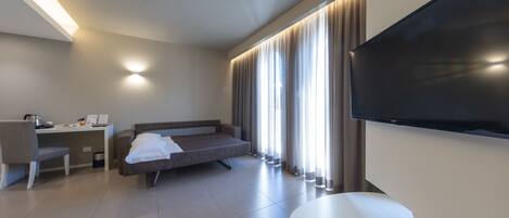 A modern hotel room with a flat-screen TV, a sofa, a desk, and a chair.