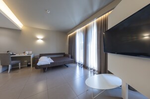 A modern hotel room with a flat-screen TV, a sofa, a desk, and a chair.