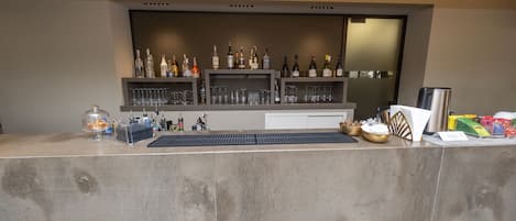 A bar area with shelves of liquor bottles and glasses, a bar counter, and a cash register.