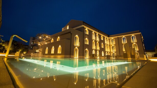 A large building with a swimming pool at night, featuring multiple windows and a well-lit exterior.