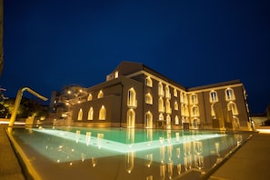 Un edificio grande con piscina por la noche, con varias ventanas y un exterior bien iluminado.