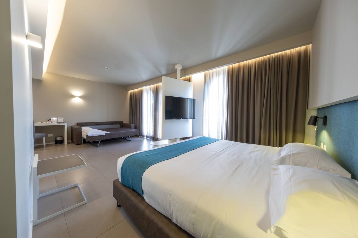 Ein modernes Hotelzimmer mit einem großen Bett, einem Flachbildfernseher, einem Schreibtisch und einer Sitzecke.