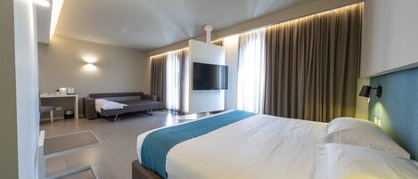 A modern hotel room with a large bed, a flat-screen TV, a desk, and a sofa.