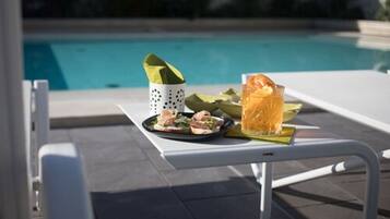 A dining table with a meal and a drink by a poolside.