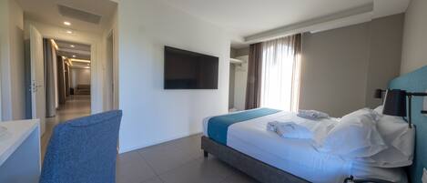 Habitación de hotel con cama, escritorio, silla, televisor y teléfono sobre la mesita de noche.