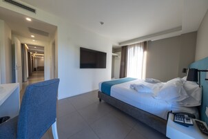 Habitación de hotel con cama, escritorio, silla, televisor y teléfono sobre la mesita de noche.