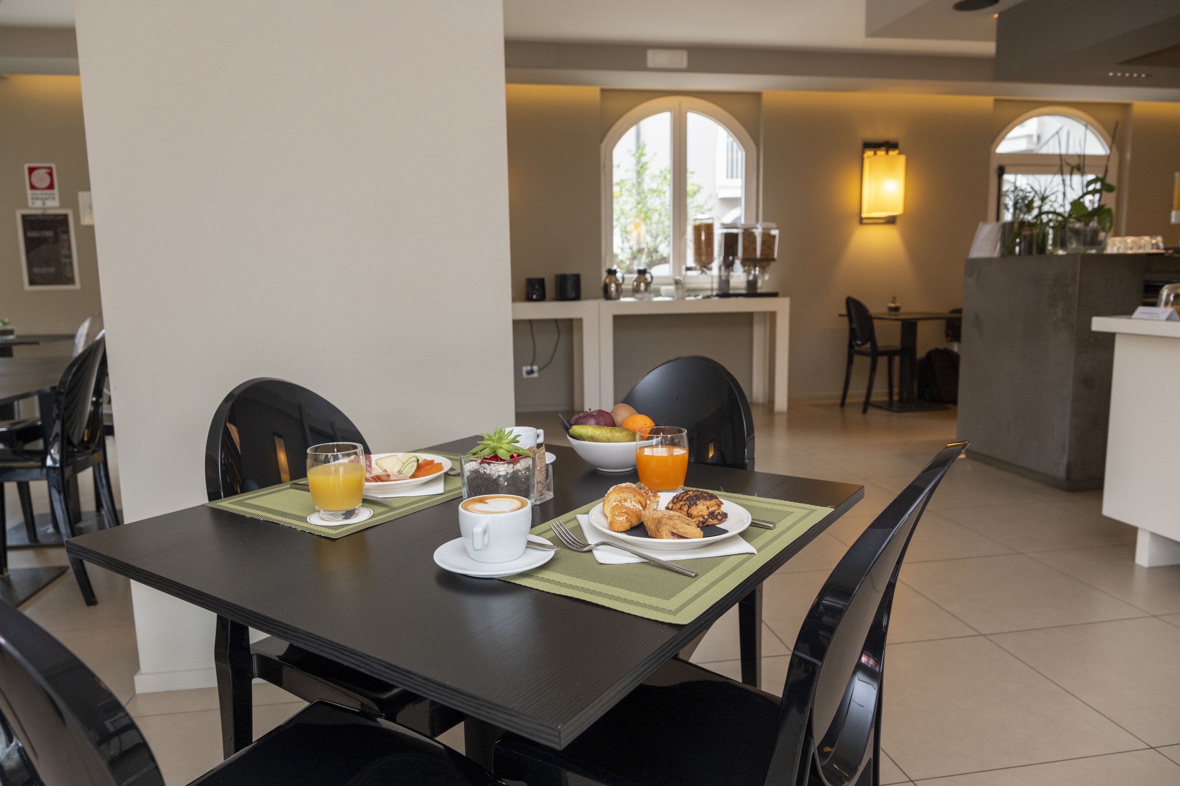 Un comedor con una mesa dispuesta para el desayuno, que incluye cruasanes, una taza de café y zumo de naranja.