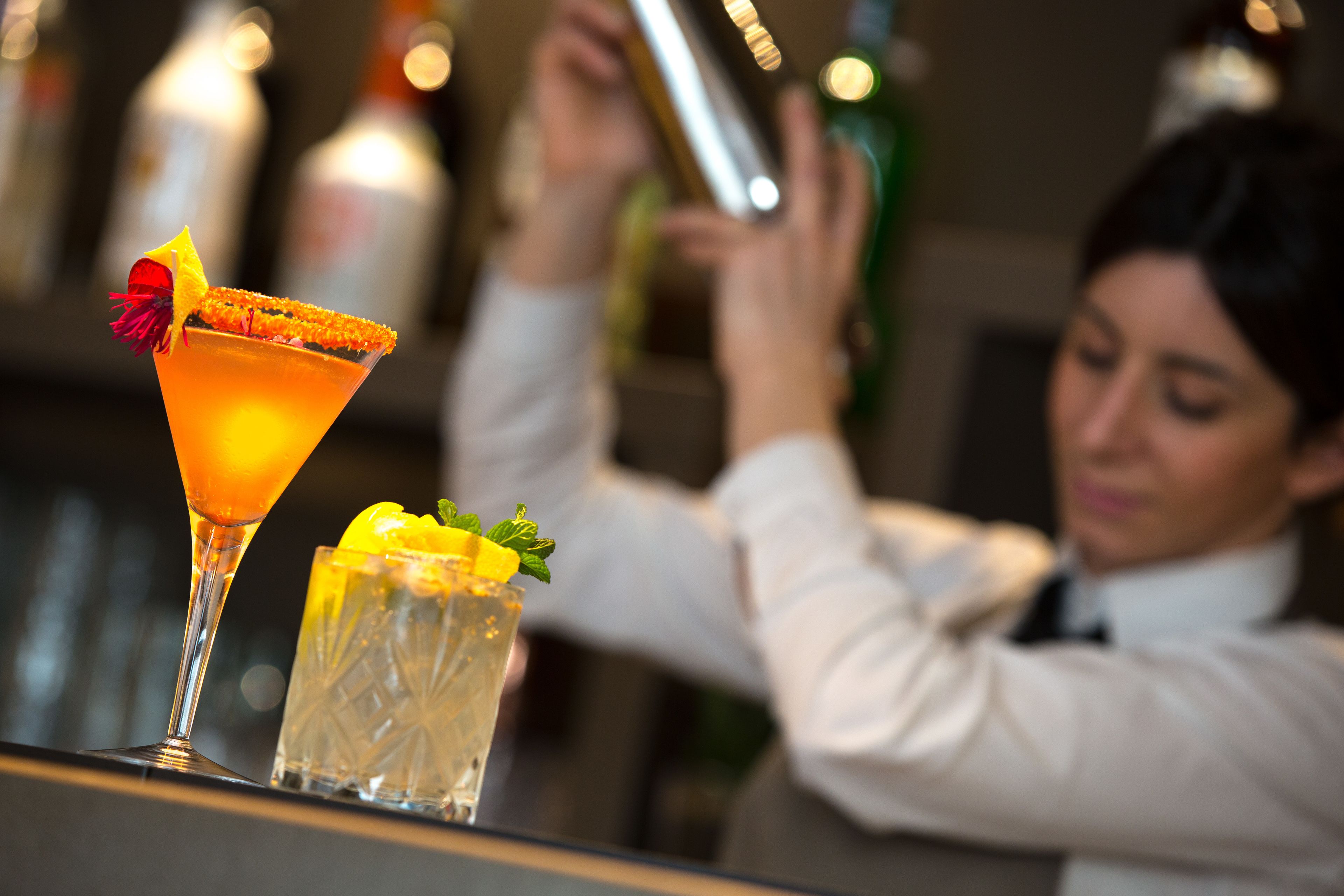 Un barista prepara cocktail dietro al bancone, con un bicchiere Martini e un bicchiere highball.