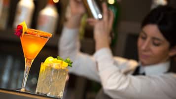Un barman prépare des boissons derrière un comptoir, avec un verre à martini et un grand verre droit.