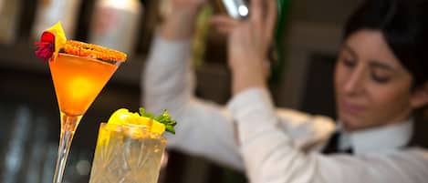 A bartender preparing drinks behind a bar with a martini glass and a highball glass.