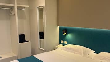 A modern hotel room with a large bed, a built-in wardrobe, a mirror, and a nightstand with a lamp.