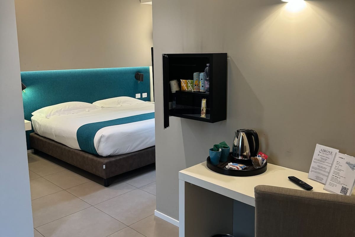 Ein Hotelzimmer mit einem Bett, einem Schreibtisch mit Fernbedienung, einem Papierkorb und einem Wandregal mit Pflegeartikeln.