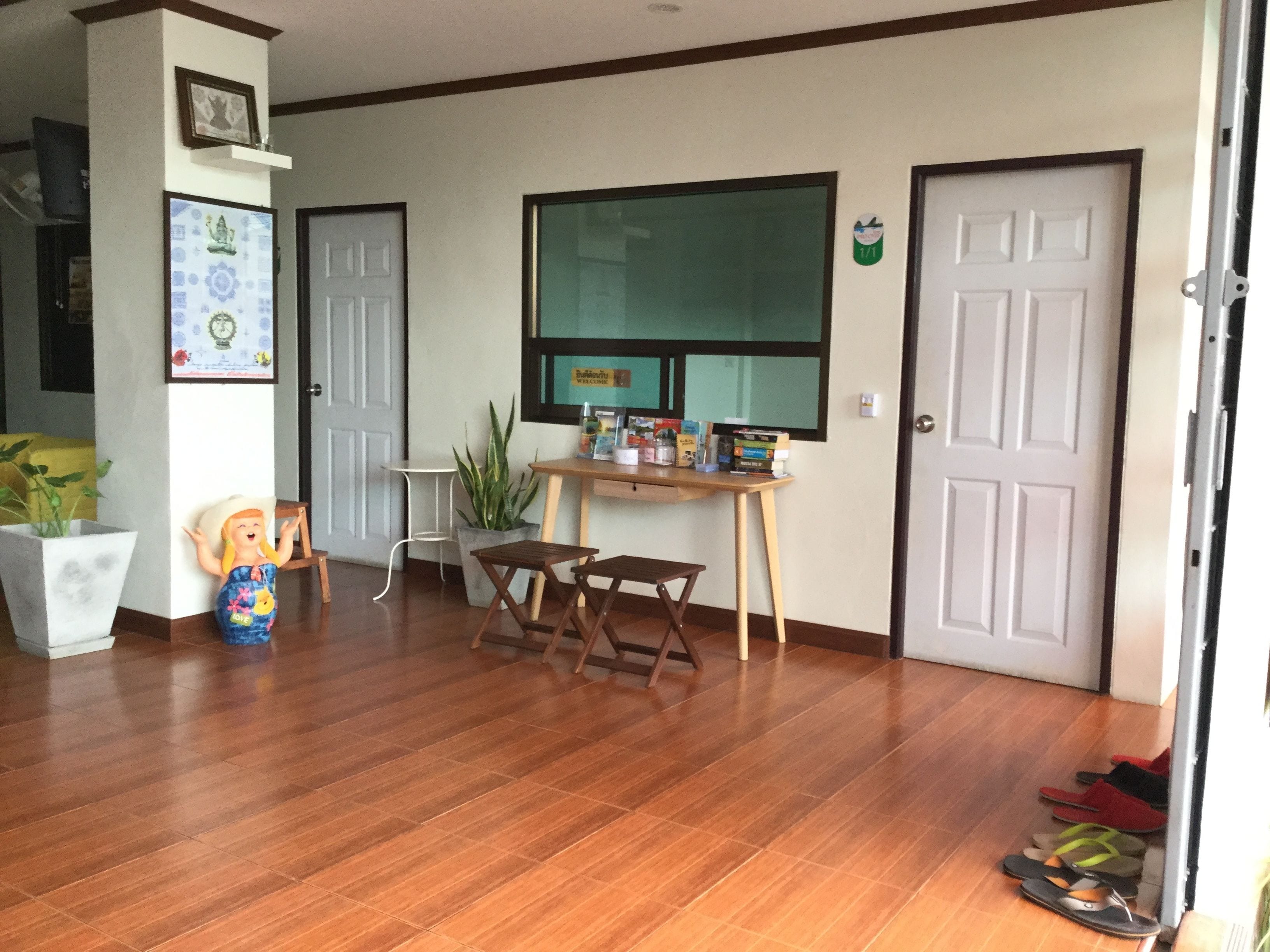 A room with wooden flooring, a desk with books, a chair, a potted plant, and a door with a sign.