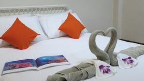 Een opgemaakt bed met witte en oranje kussens, een handdoekzwane in de vorm van een hart, en een boek op het bed.