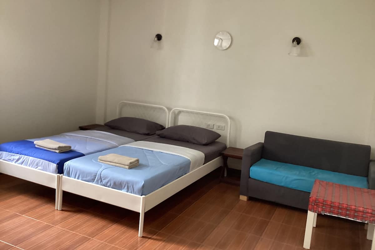 Un dormitorio con dos camas individuales, un sofá gris y una mesita con mantel rojo.