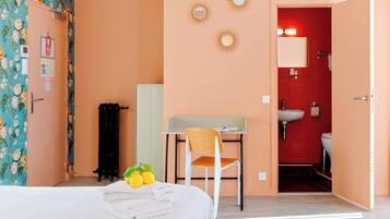 Ein Hotelzimmer mit Bett, Schreibtisch, Stuhl und einem Badezimmer mit roter Wand, sowie einer Tür zu einem weiteren Raum.