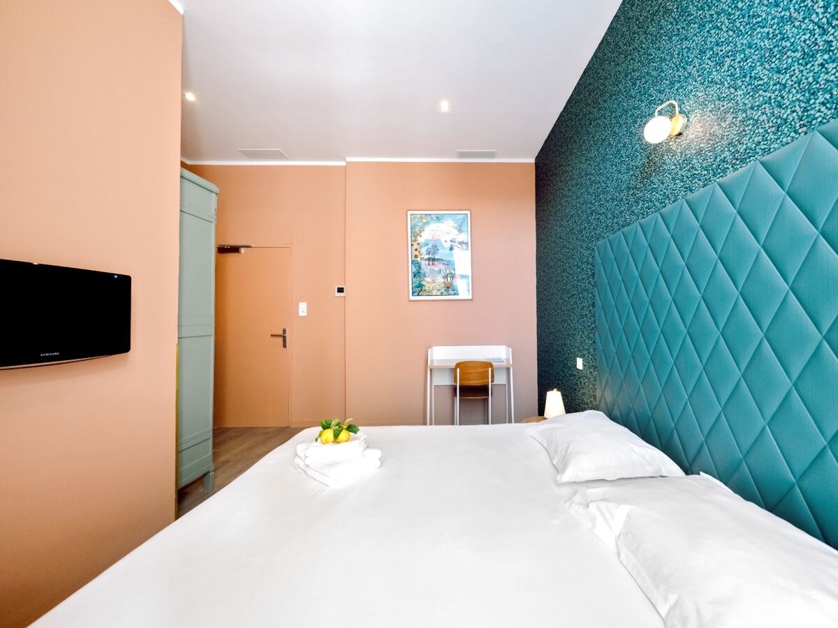 A hotel room with a large bed, a flat-screen TV, a small table with a chair, and a teal accent wall.