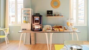 A modern kitchen with a coffee machine, a refrigerator, and a dining area with chairs and a table. - Hôtel Lemon (Menton)