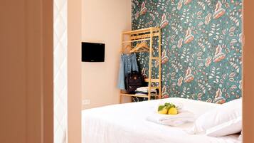 Un dormitorio con cama, perchero de madera, televisor montado en la pared y papel tapiz estampado.