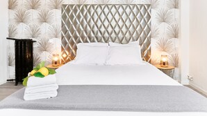 A neatly made bed with white linens, a grey throw blanket, and a decorative arrangement of towels and lemons on the foot of the bed. - Hôtel Lemon (Menton)
