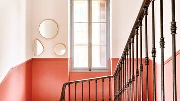 A staircase with a black balustrade, a red wall, and a window with shutters.