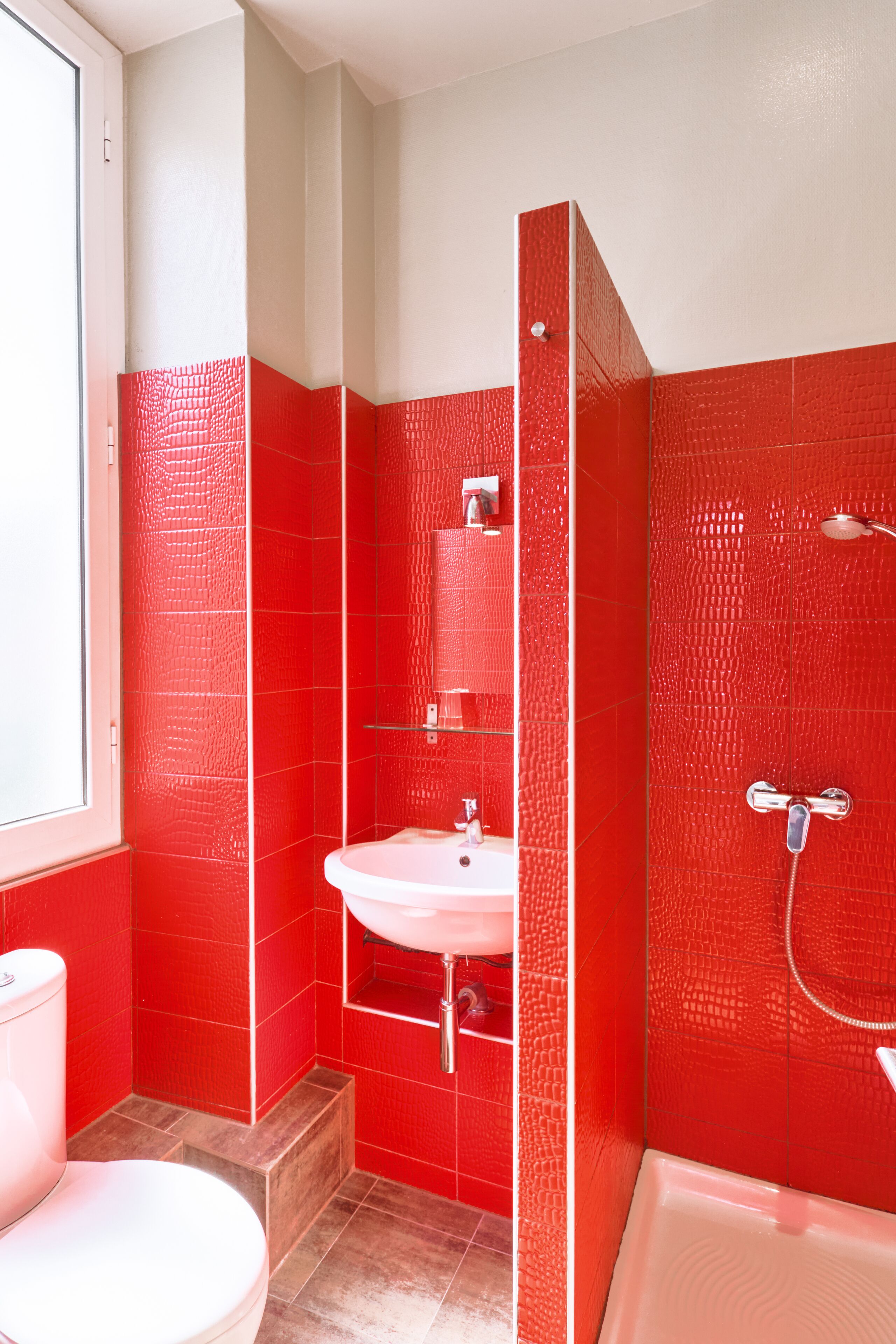 A bathroom with red tiled walls, a white sink, and a bathtub.